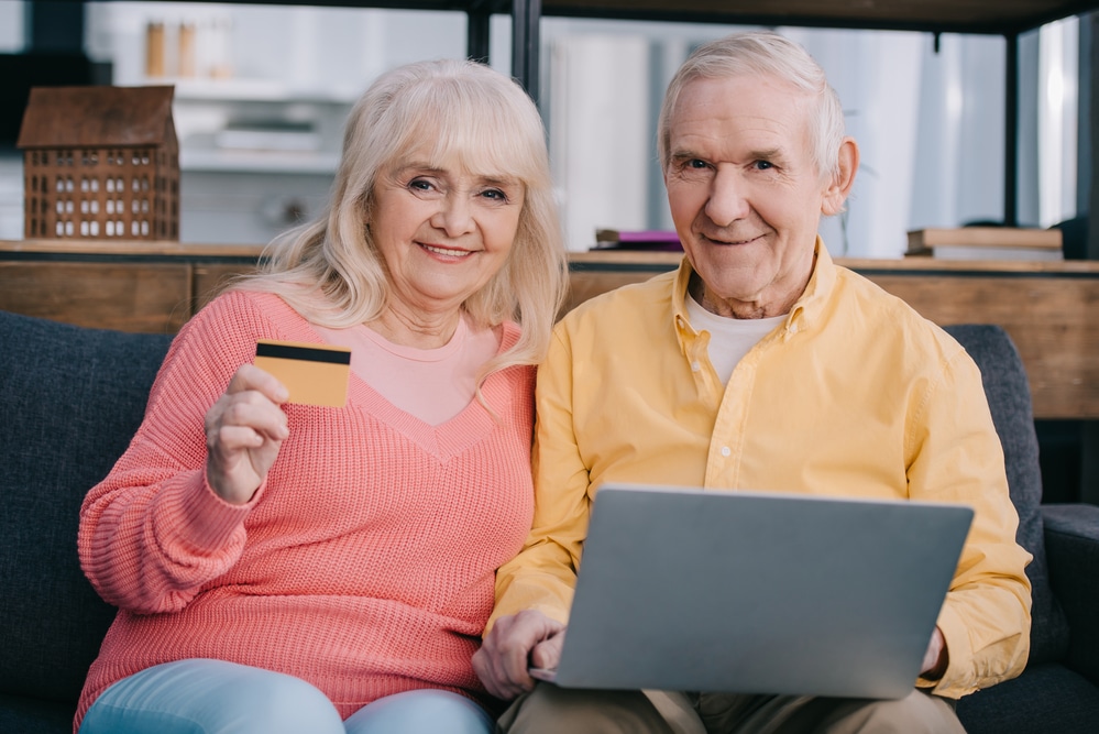 an elderly couple holding a laptop and a credit card